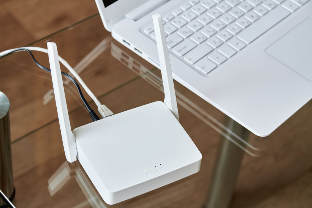 White wireless wi-fi router near a laptop on a glass table